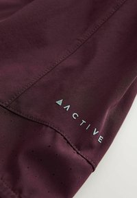 Bordo atletski materijal s glatkom teksturom; sadrži perforacije i svijetloplavi logo s natpisom "ACTIVE" blizu ruba.