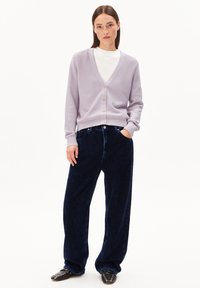 Licht paarse gebreide cardigan met een V-hals en knoopsluiting, gecombineerd met marineblauwe corduroy wijde broek en zwarte loafers met studs.