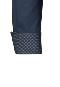 Manica di camicia da dress navy in tessuto testurizzato; il polsino presenta un bordo a motivo scuro con piccole forme geometriche ripetute e bordi lisci.