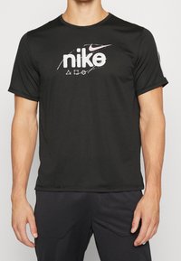 Black Nike short-sleeve t-shirt features a large white logo and graphic accents. Made from moisture-wicking fabric with a smooth texture.