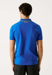 Niebieska koszulka polo z kontrastowym żółtym kołnierzykiem, krótkimi rękawami, gładką teksturą i logo "PEPE JEANS" na karku.