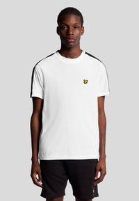 Vit bomull t-shirt med svarta axelstrimmor och en liten gul logotyp på bröstet. Kort ärm och rundad halsdesign.