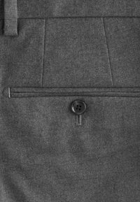 Gros plan sur un pantalon en tissu gris avec un seul bouton noir sécurisant une poche arrière avec une ouverture fendue horizontale.