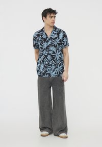 Camicia nera a maniche corte con motivo di foglie di palma blu chiaro, abbinata a jeans scuri a gamba larga e scarpe beige. Design del colletto semplice.