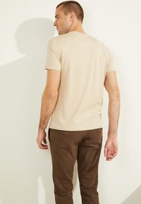 Beež puuvillane T-särk lühikeste käistega ja ümmarguse kaelusega, millele on sobitatud tumepruunid püksid, millel on tagataskud ja sile tekstuur.