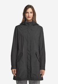 Svart vattentät jacka med hög krage, långa ärmar och fickor på sidan med tryckknappar. Slät textur och avslappnad passform, lämplig för olika väderförhållanden.