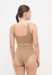 Set di reggiseno sportivo color tan e slip alta vita. Tessuto morbido e elastico con spalline larghe e design minimalista. Senza fantasie o accessori.