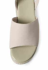 Beige neplederen slip-sandaal met een brede bovenband, ronde neus en een groene zool. Gladde textuur met minimale stiksel details.