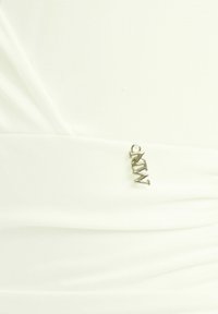 Tessuto bianco dal tocco morbido, con dettagli arricciati. Un accento di logo metallico è attaccato vicino alla cucitura per un ulteriore elemento di design.