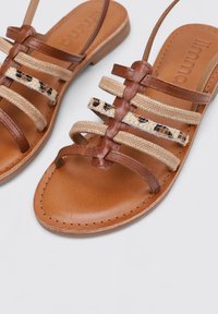 Sandalias de cuero marrón con múltiples correas de lienzo beige y acentos de estampado animal. Textura suave, punta redondeada y diseño de suela plana.