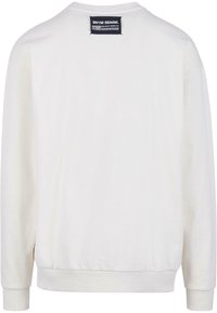 Sweat-shirt blanc à manches longues avec poignets et ourlet côtelés, comportant une étiquette rectangulaire noire avec texte blanc près du col arrière.