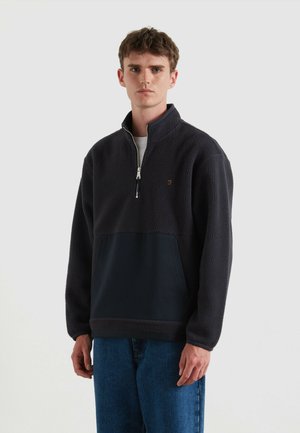 Pullover in pile di colore blu scuro con mezza zip, dotato di un pannello liscio nella parte inferiore; parte superiore texturizzata e logo discreto sul petto.