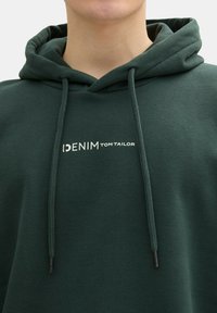Zelená bavlnená mikina s kapucňou a šnúrkou na krku, so štýlovým bielym potlačeným logom "DENIM TOM TAILOR" na prednej strane. Mäkka textúra a ležérny dizajn.