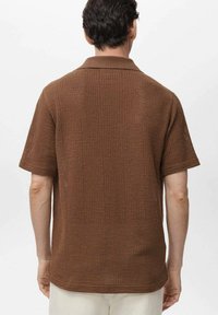 Brown knitted short-sleeve shirt featuring a polo collar and textured mesh design, with a relaxed fit and straight hemline.
