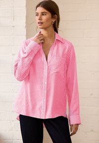 Pink striped button-up shirt with a pocket and fold-down collar. Features long sleeves with button cuffs and a relaxed fit.
