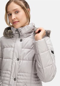Jasnoszara kurtka puchowa o teksturowanym wykończeniu, z kapturem wykończonym futrem, guzikami z przodu oraz pikowanym wzorem. Posiada logo na rękawie.