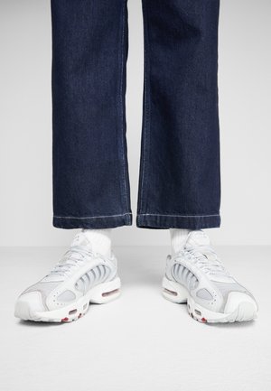 Person iført hvide atletiksneakers med synlig luftpolstring og hvide sokker, kombineret med mørkeblå viddebenede denimjeans.