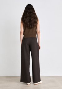 Maglione senza maniche marrone abbinato a pantaloni larghi scuri. L'outfit presenta una vita aderente e una consistenza liscia, che si completa con scarpe bianche sporche.