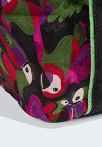 Esquina de una bolsa con ilustraciones de aves tropicales brillantes en rojo, púrpura, verde y negro sobre una tela texturizada con un borde verde.