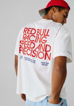 Weißes T-Shirt mit auffälligem rotem Text auf der Rückseite, der "RED BULL RACING SPEED AND PRECISION" lautet, mit blauen Akzenten und Logodetails.