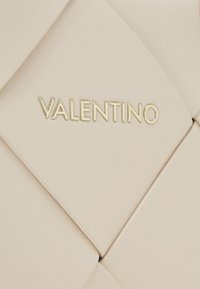 Beige läderhandväska med kviltad design och guld "Valentino"-logotyp. Slät textur med framträdande sömmar och subtil glans.