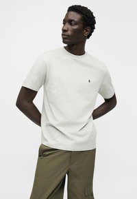 T-shirt à manches courtes gris clair en mélange de coton, avec un col rond et un petit logo noir sur la poitrine.