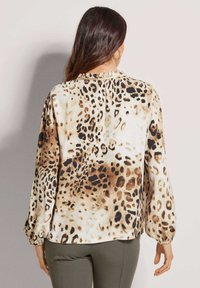 Blouse met luipaardpatroon van zachte stof, lange pofmouwen, een gerimpelde halslijn en tinten beige, bruin en zwart in het patroon.