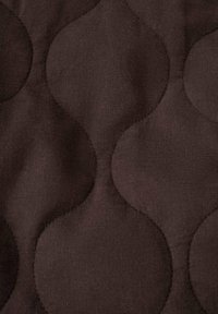 Dunkelbrauner Stoff mit einem strukturierten Muster aus großen, sich überlappenden Kreisen. Das Material wirkt weich und glatt mit präzisen Nähdetails.