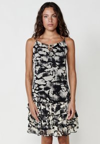 Schwarz-beige gemustertes Kleid mit gerafftem Saum, verstellbaren Spaghettiträgern und einem Schlüssellochdetail am Ausschnitt.