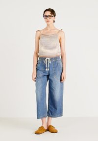 Top cu dungi, cu bretele subțiri, asortat cu pantaloni din denim cu picioare largi, având talie elastică și șnur. Încălțăminte slip-on maro.