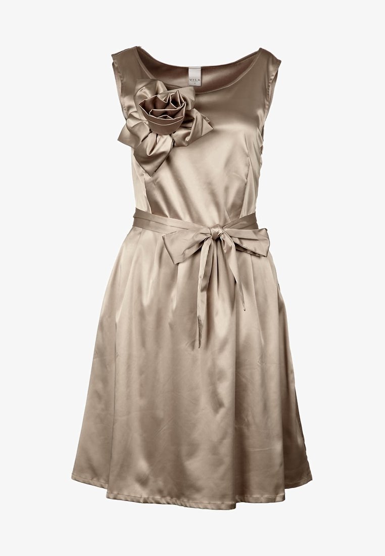 Satin beige klänning med en figursydd överdel, breda axlar och en stor blomma som accent. Har en midja med bälte och en A-linjär kjol.