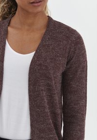 Cardigan en maille bordeaux avec une légère texture, à ouverture devant et à manches longues, superposé à un t-shirt blanc à col rond.