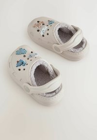 Sabots gris clair avec doublure en polaire, ornés de breloques décoratives en forme d'animaux de couleur bleue, marron et blanche. Bride arrière ajustable incluse.