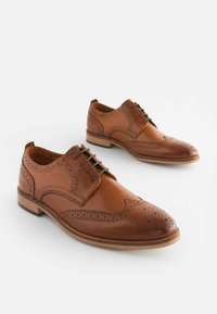 Zapatos brogue de cuero marrón con detalles perforados intrincados, diseño clásico de cordones y un tacón de madera. Textura suave con acabado pulido.