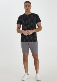 Camiseta negra con patrón de puntos blancos, de mangas cortas. Pantalones cortos grises y zapatillas blancas. Ajuste casual, tejido suave y detalles mínimos.
