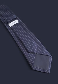 Stripet marineblå slips med tynne hvite striper. Laget av glatt stoff, med en spiss ende og en merkelapp sydd på den smale enden.