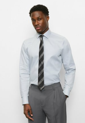 Hellblaues Langarmhemd mit Kragen, kombiniert mit einer grauen plissierten Anzughose und einer schwarz gestreiften Krawatte. Glatte Textur und maßgeschneiderte Passform.