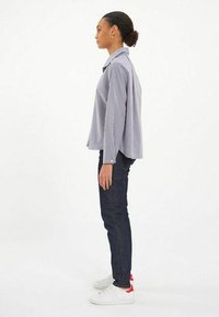 Chemise à rayures bleu clair et blanche, coupe décontractée, associée à un jean en denim foncé et des baskets blanches avec des accents rouges.
