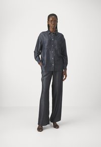 Set di camicia in denim scuro e pantaloni a gamba larga, caratterizzato da una texture morbida, chiusura con bottoni e una leggera lucentezza. Completa il look con sandali con la punta aperta.