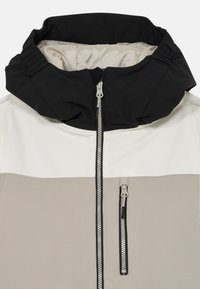 Värviblokeeritud jakk, millel on must kõrge kaelus, helesinised ja beeži paneelid ning täispikk tõmblukk koos kontrastse tõmbluku tõmbega.