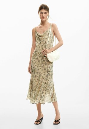 Cowl-hals, ærmeløs kjole i lys beige med blomstermønster, flydende stof og kontrasterende sort kant. Kombineret med en hvid taske og sorte hæle.