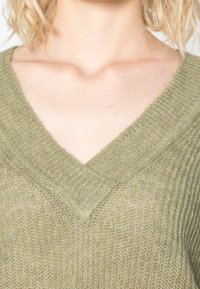 V-Ausschnitt Strickpullover in hellem Olivgrün, aus einem strukturierten, weichen Stoff. Mit geripptem Ausschnitt und lockerem, entspanntem Schnitt.
