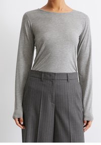 Langärmliges graues Oberteil aus weichem Stoff, kombiniert mit grauen Nadelstreifen-Hosen. Das Oberteil hat einen runden Ausschnitt und enganliegende Ärmel.