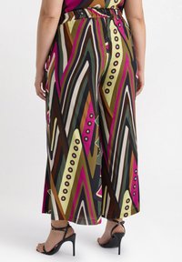 Breda byxor i flerfärgad zigzag-mönster med djärva ränder, elastisk midja och slät tyg. Kombination med svarta högklackade sandaler.
