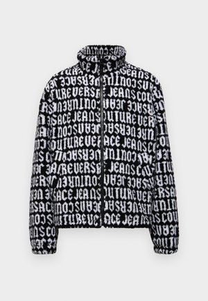 Veste noire et blanche floue avec col montant, fermeture zippée et impression textuelle sur l'ensemble. Texture douce et design court.