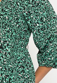 Vihreä eläinkuosisekoitteinen kangasmekko mustavalkoisilla yksityiskohdilla, jossa on poimuttu pääntie ja puffyhihat, teksturoitu sileällä viimeistelyllä.