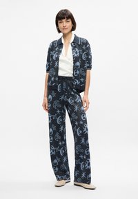 Tenue bleu marine avec des motifs célestes blancs ; comprend une chemise à manches courtes à boutons et un pantalon large. Présente une texture douce.