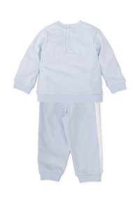 Chándal de algodón azul claro que incluye una camiseta de manga larga con detalles de botones y pantalones a juego con franjas laterales blancas. Textura suave en todo.