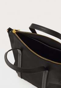 Musta nailoninen olkalaukku kultaisella vetoketjulla, joissa on kaksi yläkahvaa ja struktuuripinta. Sisätila on tilava ja vuorattu tummalla värillä.