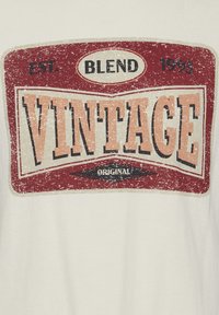 Tricou alb cu un grafic în stil vintage, în nuanțe de roșu, bej și negru. Textul spune "BLEND EST. 1993 VINTAGE ORIGINAL" cu un finisaj uzat.